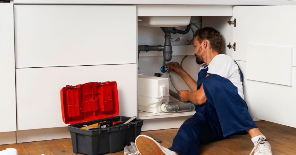 Plumber working under a kitchen sink cabinet with tools, repairing plumbing pipes and drainage system